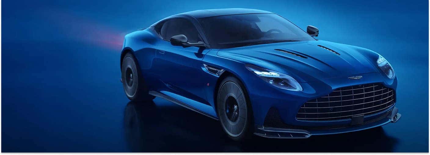 Front three-quarter view of a blue 2026 Aston Martin DB12 coupe in a studio setting.