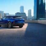 Rear exterior view of a dark blue 2025 Cadillac LYRIQ parked on the top of a parking garage surrounded by a city skyline during the day