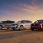 Three Cadillac XT6 models parked next to each other on a dirt road with a sunset in the background