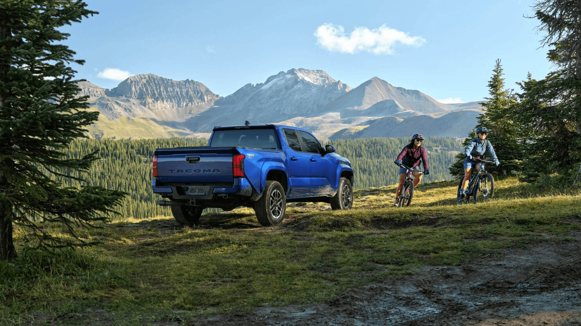 Landscape image of the 2024 Toyota Tacoma next to two bikers in the woods