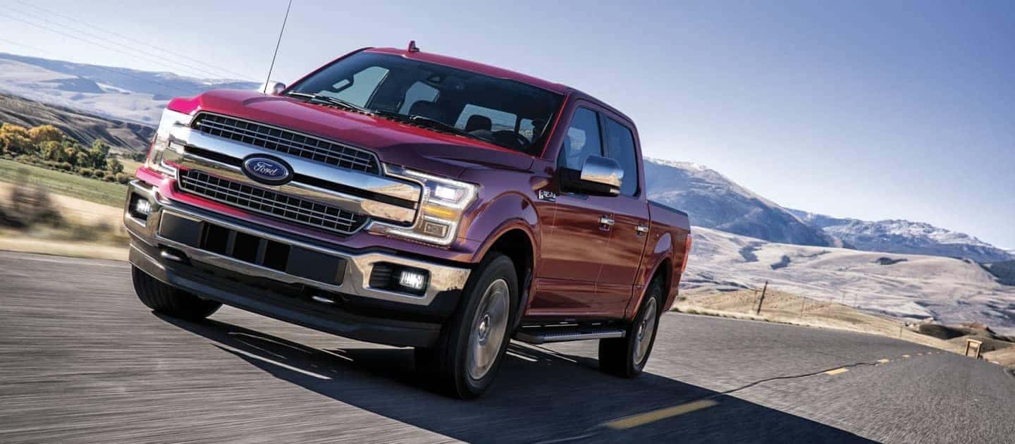 red Ford F-150 driving on highway with mountains in the background