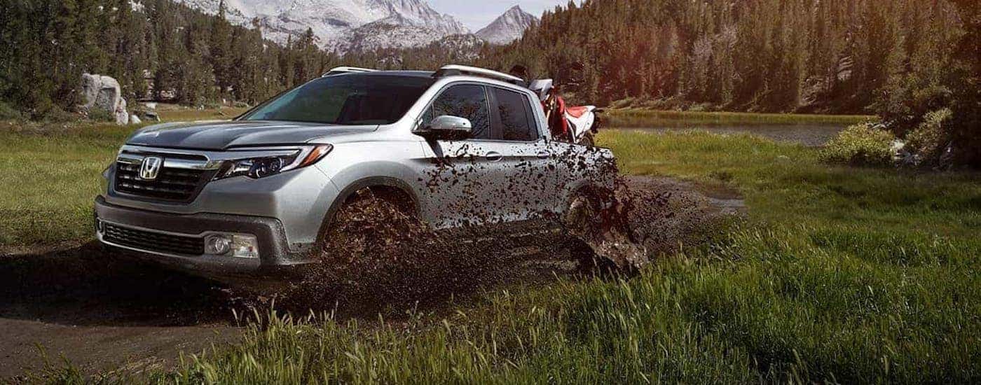 A silver 2020 Honda Ridgeline AWD RTL-E with dirtbike in the bed is shown splashing through mud.