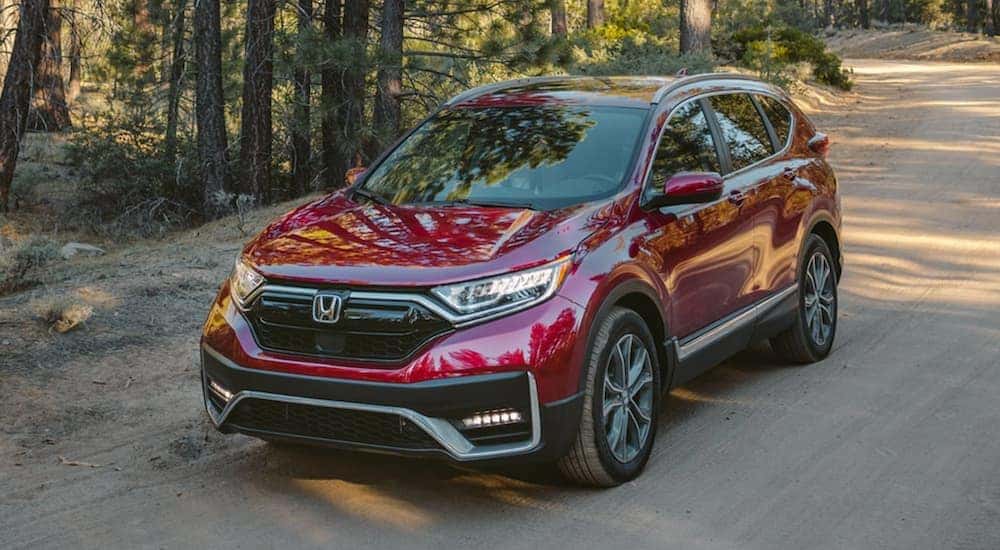 A dark red 2020 Honda CR-V Hybrid Touring is driving on a dirt road.