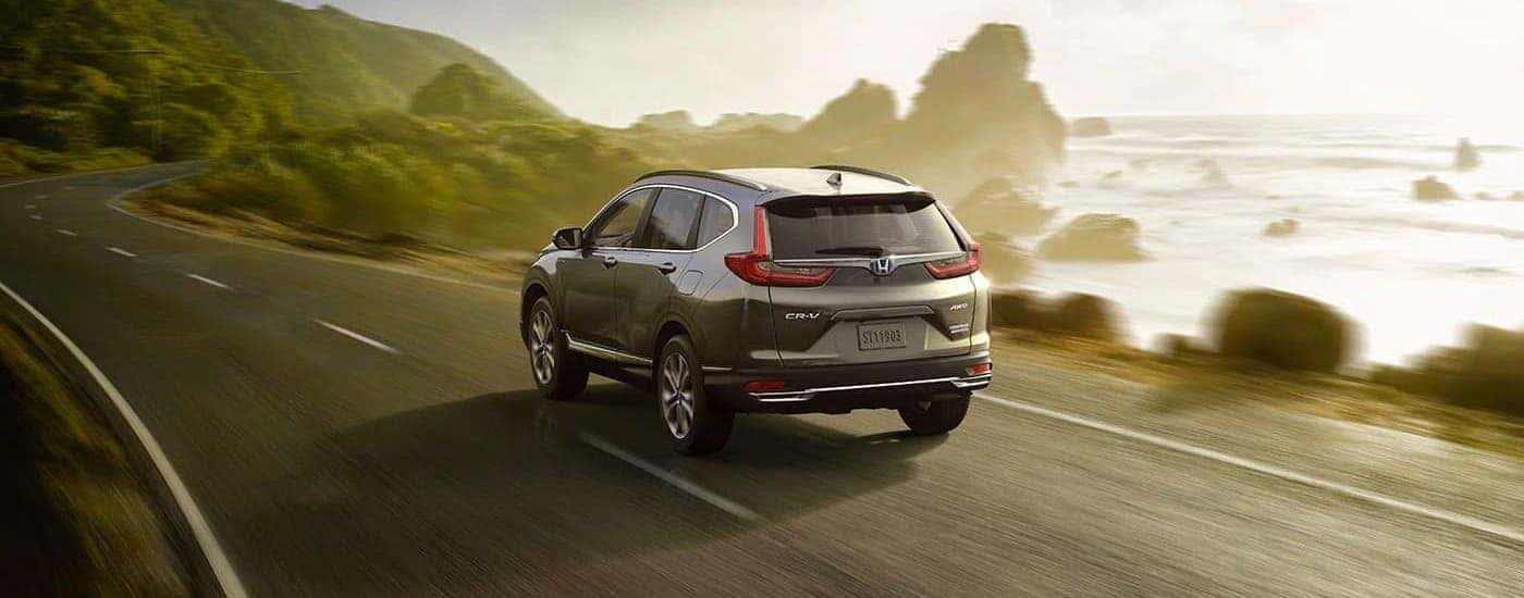 A gray 2020 Honda CR-V Hybrid Touring is shown from the rear driving along a coastal highway after winning the 2020 Honda CR-V vs 2020 Toyota RAV4 comparison.