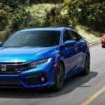 A blue and a red 2016 used Honda Civic Sedan SI are driving down a wooded raod.