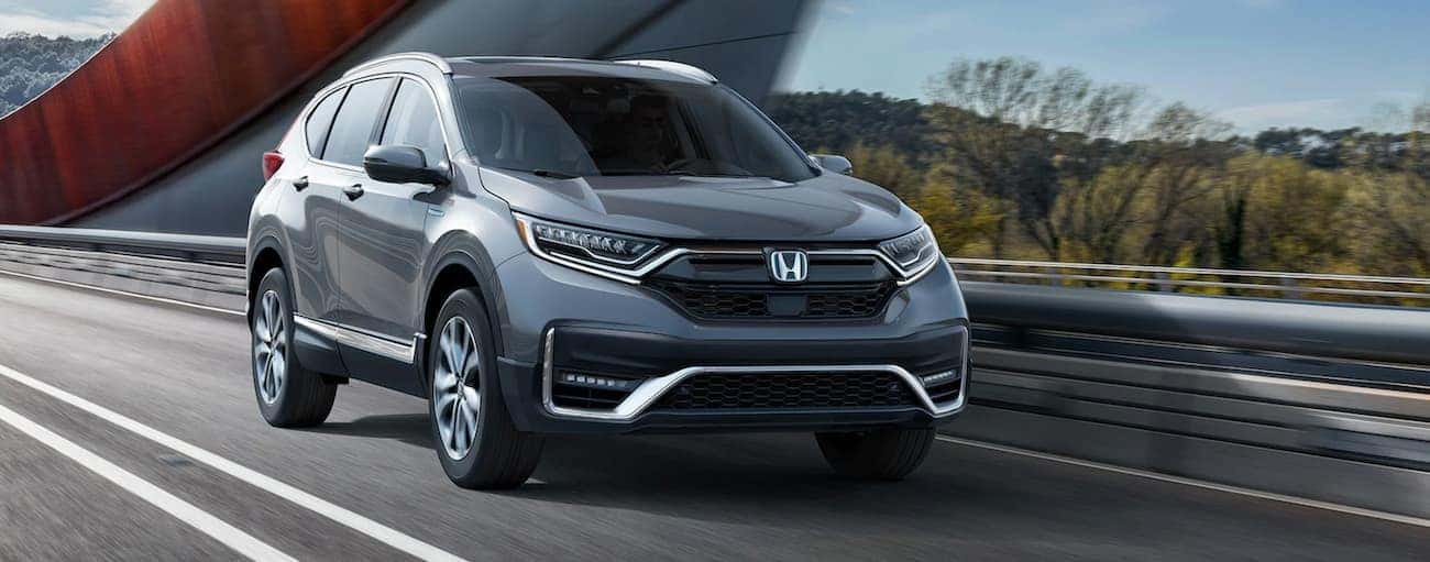 A popular 2021 Honda Hybrid, a grey CR-V Hybrid Touring is driving over a bridge.