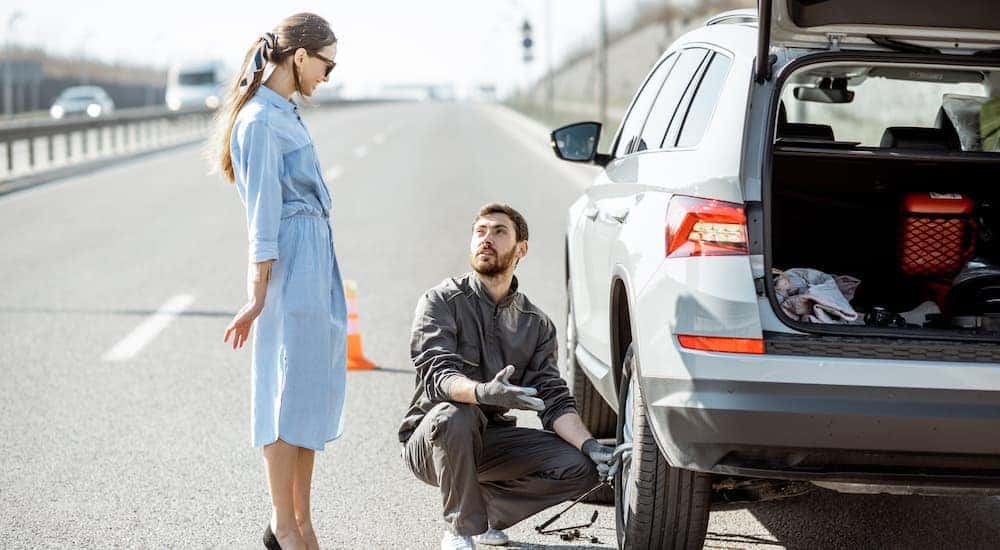 A woman is standing next to a tech changing a tire during roadside assistance.