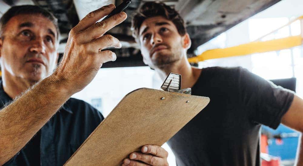 A mechanic with a clipboard is inspecting a car on a lift.