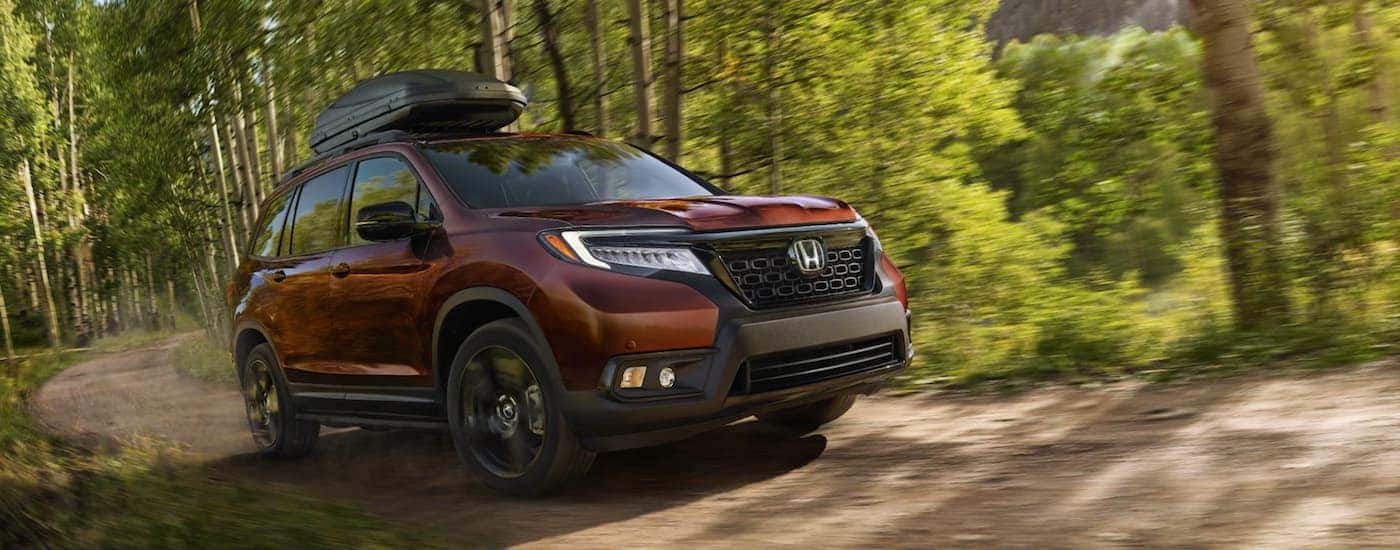 A burgundy 2021 Honda Passport Elite is driving on a dirt road in the woods.