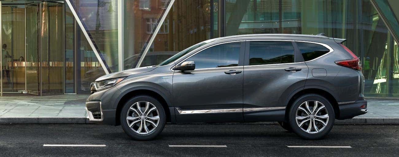 A grey 2021 Honda CR-V Touring Hybrid is shown from the side in front of a glass building.