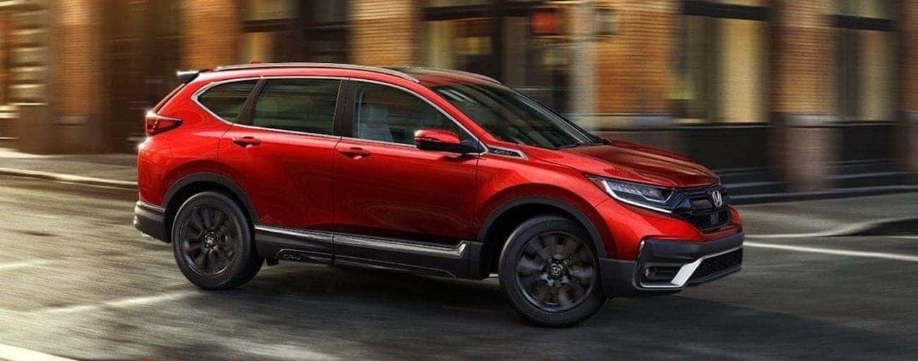 A red 2021 Honda CR-V Touring is driving on a city street after winning the 2021 Honda CR-V vs 2021 Nissan Rogue comparison.