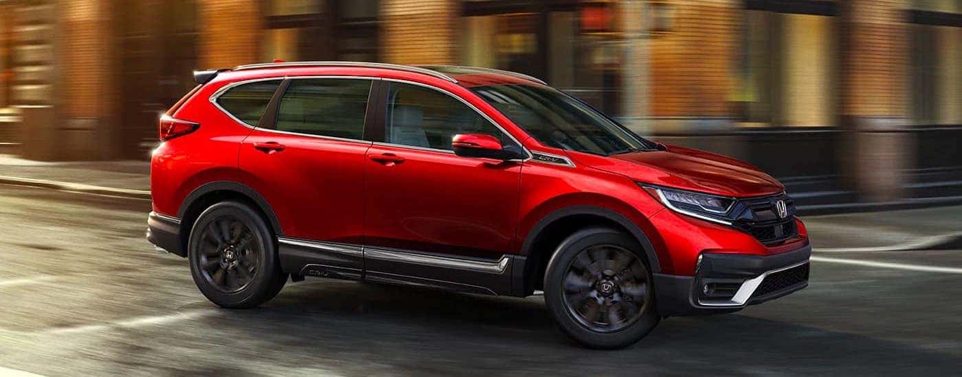 A red 2021 Honda CR-V Touring is driving on a city street.