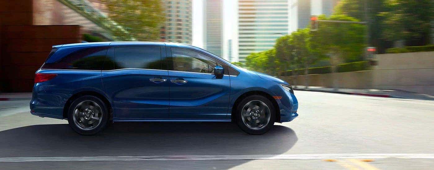 A blue 2021 Honda Odyssey is shown from the side driving on a city street after leaving a Honda dealership in Atlanta.
