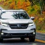 A white 2020 used Honda Pilot is shown from the front driving down a twisty road.