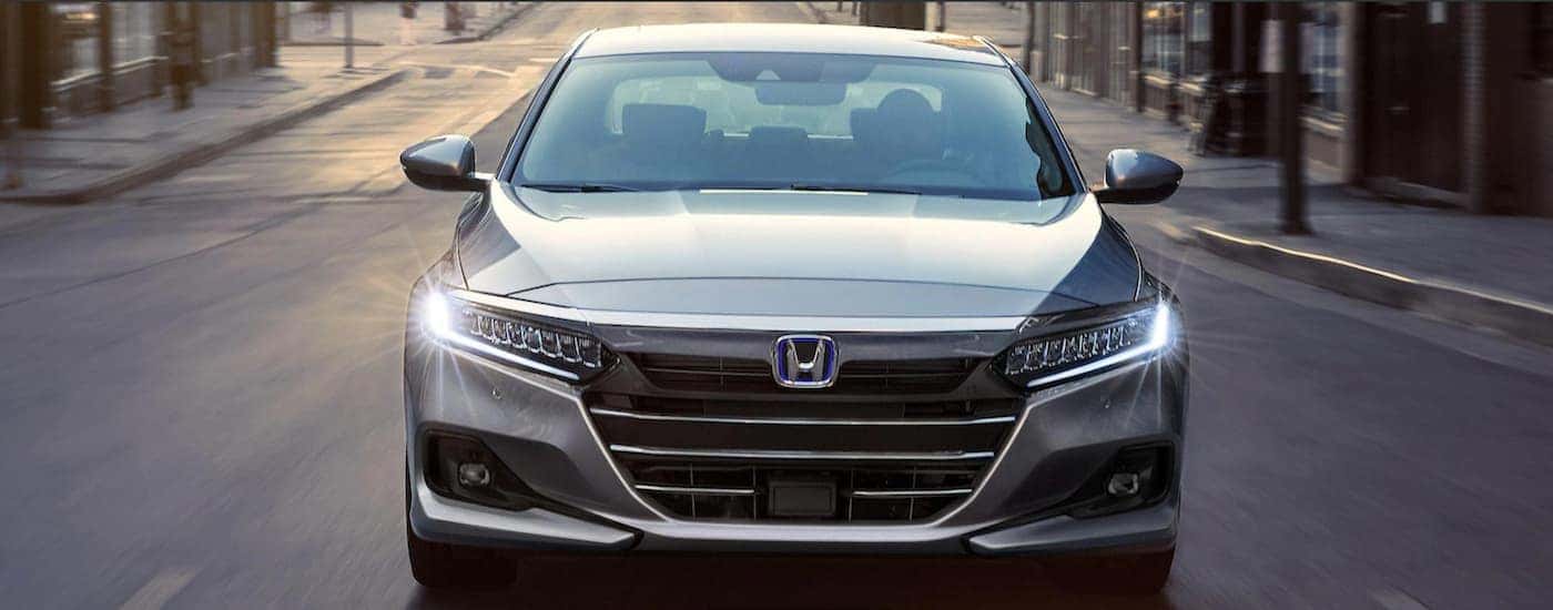 A gray 2021 Honda Accord hybrid is shown from the front driving through the city.