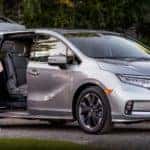 A silver 2020 used Honda Odyssey is shown from the side with the door open, parked next to a fmaily.