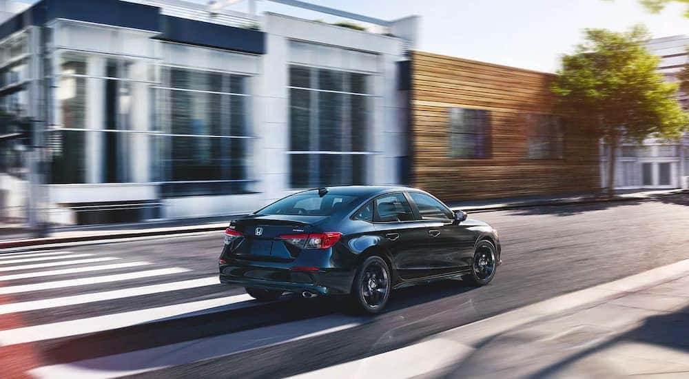 A black 2022 Honda Civic Sport is shown from behind driving through a city after leaving a 2022 Honda Civic Dealer.