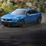 A blue 2022 Honda Civic Hatchback is shown driving down a winding road after leaving a Suwanee Honda dealer.