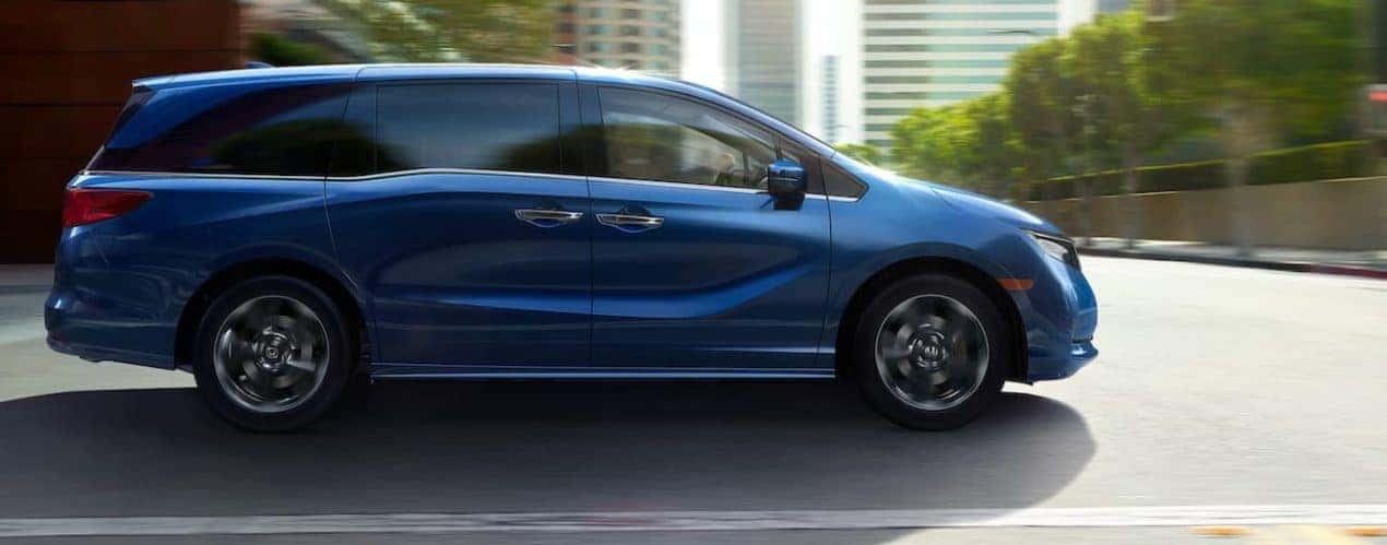 A blue 2022 Honda Odyssey Elite is shown from the side driving through a city.