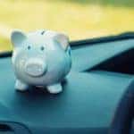 A white piggy bank is shown on the dashboard of a car.