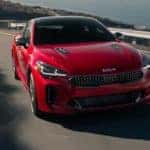 A red 2021 Kia Stinger is shown leaving a used luxury car dealer.