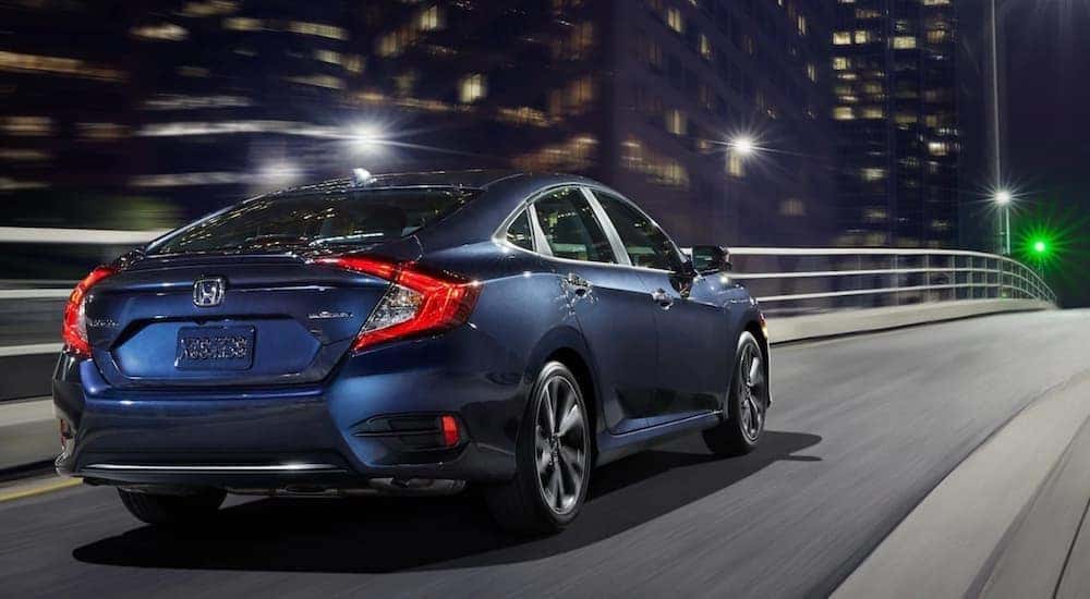 A blue 2020 Honda Civic Sedan is shown from the rear driving on a city street.