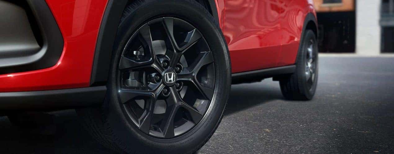 A close up shows the black alloy wheel on a red 2023 Honda HR-V Sport.