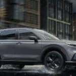 A grey 2023 Honda CR-V Sport Touring Hybrid is shown driving through a city.