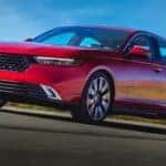 A red 2023 Honda Accord for sale is driving on a street.