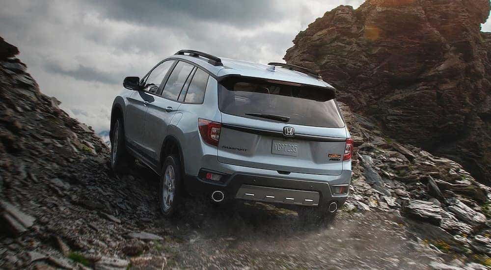 A grey 2022 Honda Passport TrailSport is shown driving up a rocky trail.