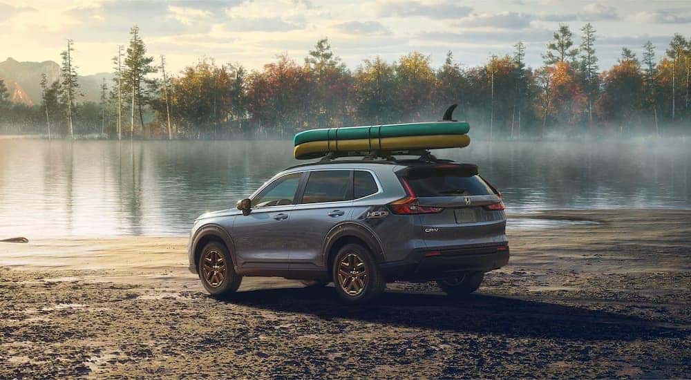 A grey 2023 Honda CR-V HPD EX is shown in front of a lake with kayaks on the roof.