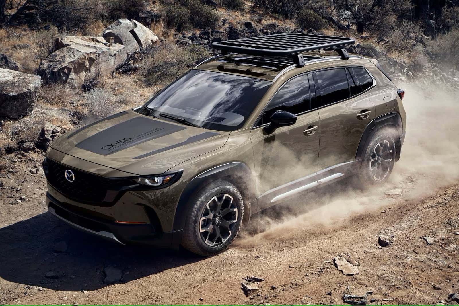 2025 Mazda CX-50 Meridian Edition driving on a dirt road with a rack on top of the hood.