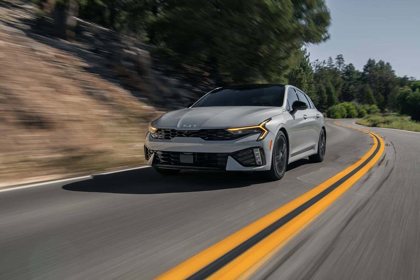 A grey 2026 Kia K5 driving down the road.