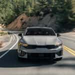 Front view of a 2025 Kia K5 driving down the road.