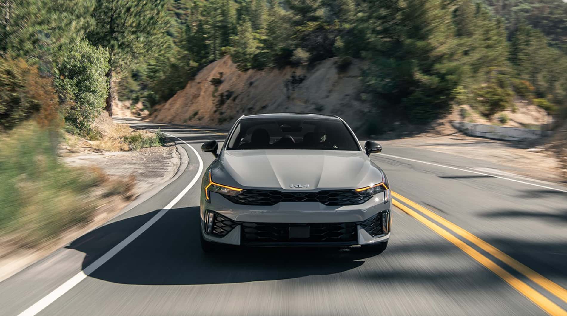 Front view of a 2025 Kia K5 driving down the road.