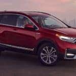 A well known Honda SUV, a red 2020 Honda CR-V Touring, is parked on a hill with a city in the distance.
