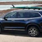 A blue 2021 Honda Pilot is parked near the ocean with a surfboard on the roof after leaving a Honda dealer near you.