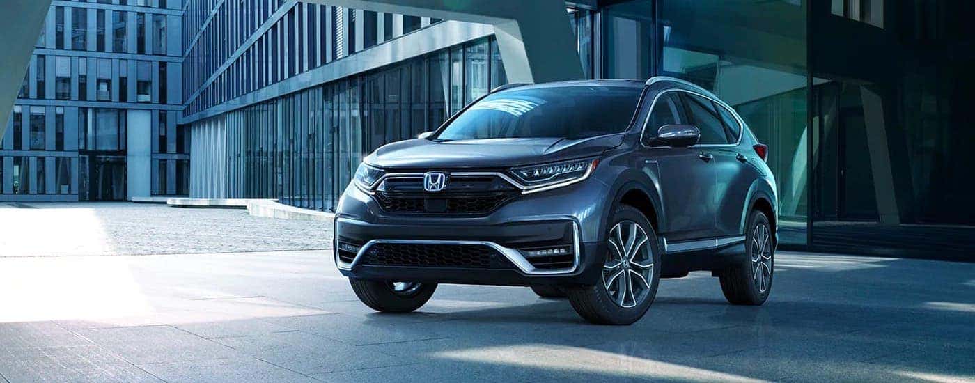 Front angled view of a blue 2021 Honda CR-V Hybrid Touring parked in front of a glass building
