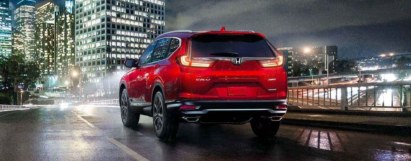 Rear view of a red 2021 Honda CR-V Touring driving on a city street in the rain