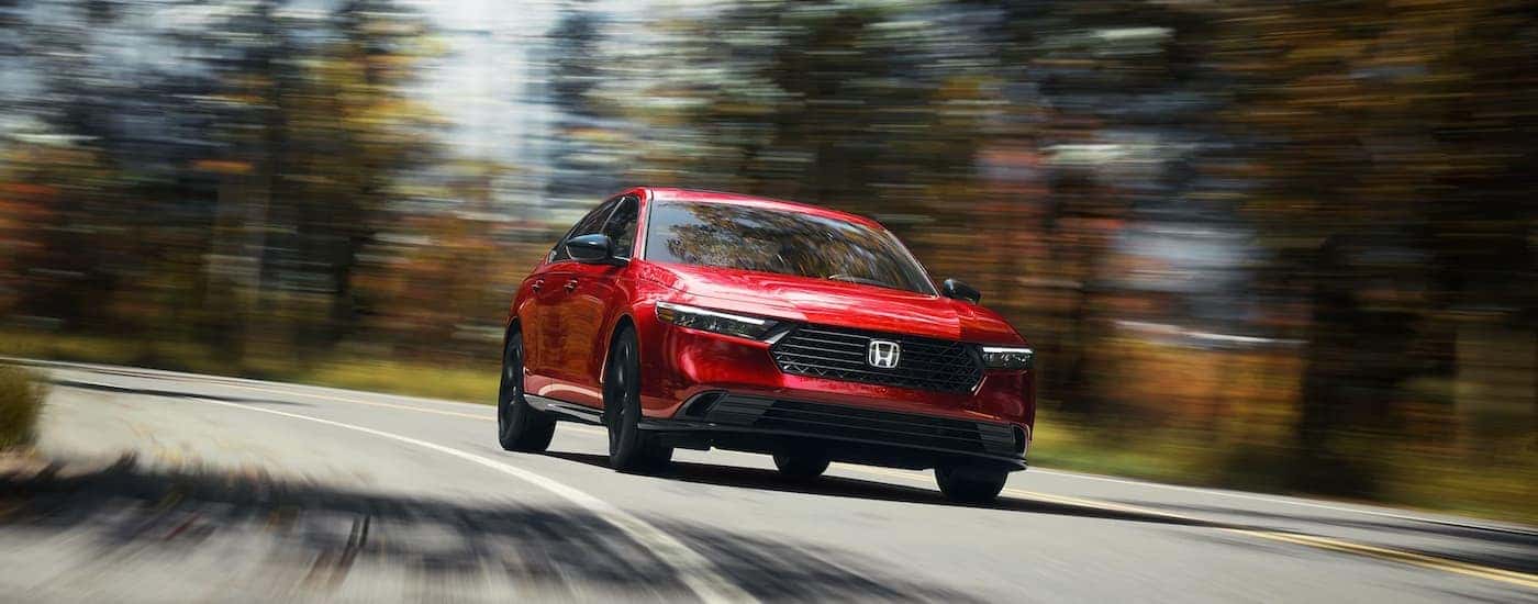 A red 2023 Honda Accord Sport L is shown speeding on a tree-lined road.
