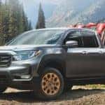 A grey 2021 Honda Ridgeline RTL-E with dirt bikes in the bed is parked in front of mountains.