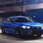 A blue 2022 Honda Civic Sport is driving on a city street at night after leaving a 2022 Honda Civic dealer.