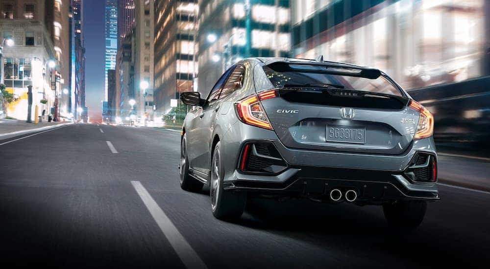 Rear view of a grey 2021 Honda Civic Sport Touring hatchback driving through the city at night