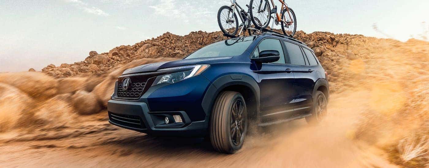 Front closeup of a blue 2021 Honda Passport Sport with bikes on the roof driving on a dirt road
