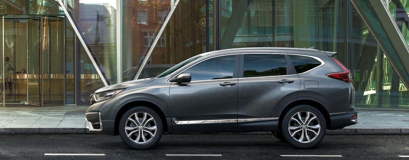 A grey 2021 Honda CR-V Hybrid Touring is shown from the side parked in front of a modern building.