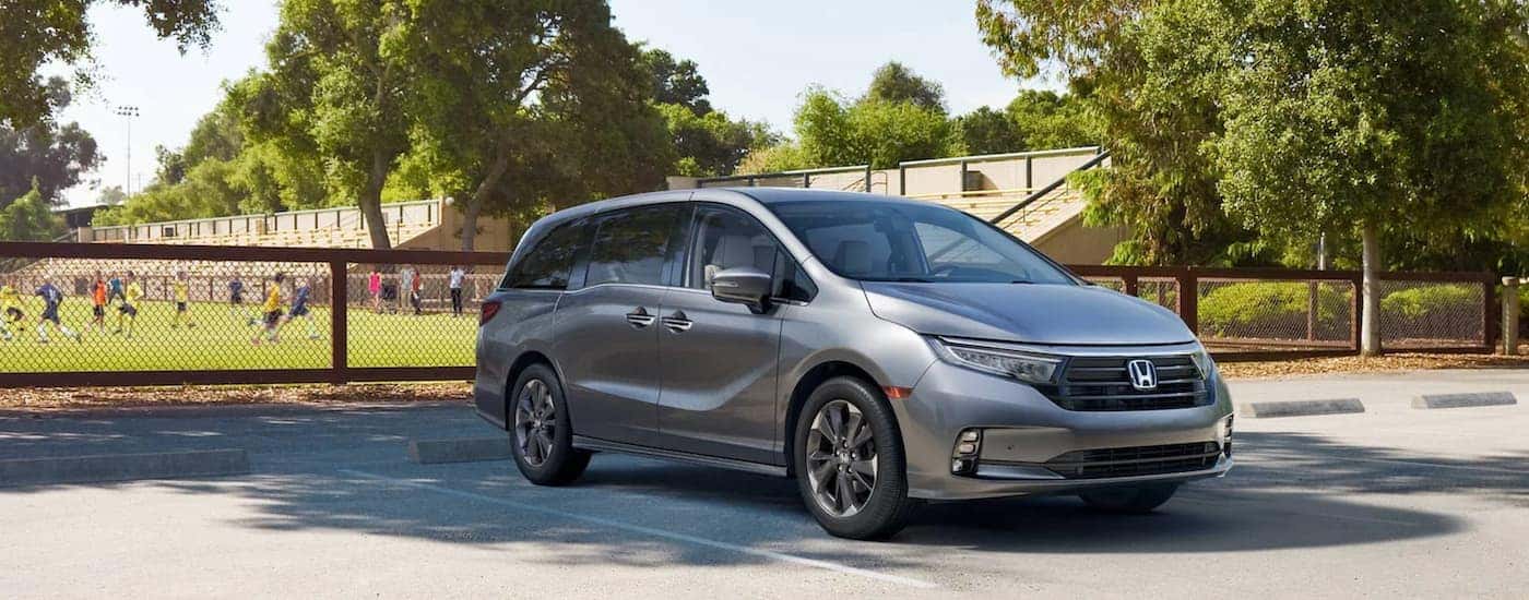 A grey 2021 Honda Odyssey is parked in front of a soccer field.