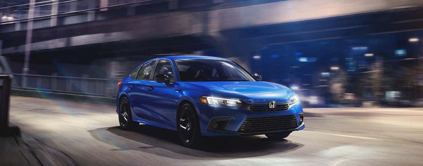 A blue 2022 Honda Civic Sport is shown from the front driving through a city.