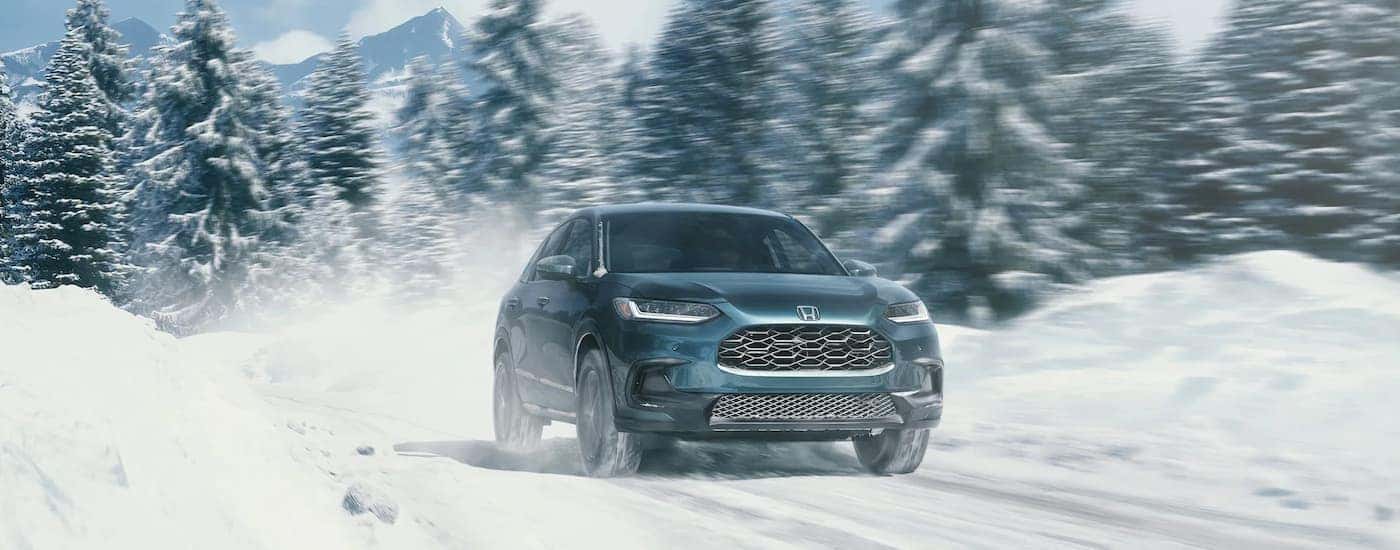 A blue 2023 Honda HR-V EX-L is shown driving on a snowy road.