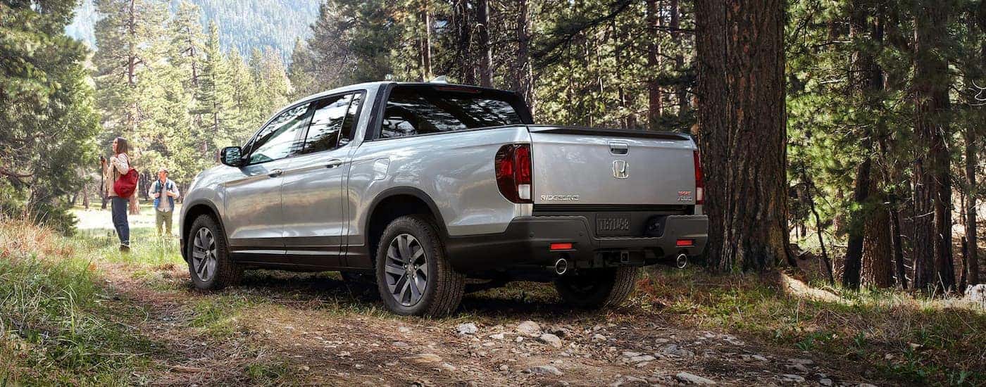 A silver 2023 Honda Ridgeline Sport is shown from the rear on a trail in the woods.