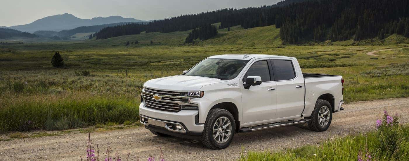 Side angled view of a white 2021 Chevy Silverado 1500 High Country driving on a dirt road
